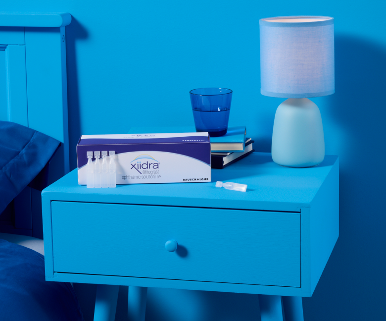 Xiidra singe use drops next to its packaging on a blue nightstand in a blue room