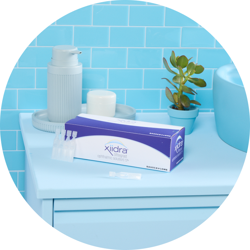 Xiidra singe use drops next to its packaging on a blue counter in a blue bathroom