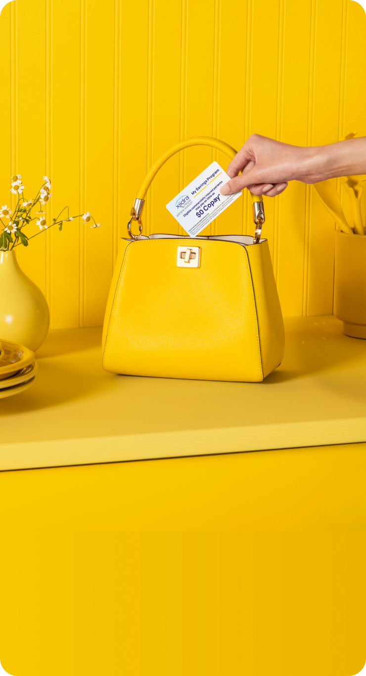 Hand holding a Xiidra Savings Program card above a yellow purse on a yellow counter
