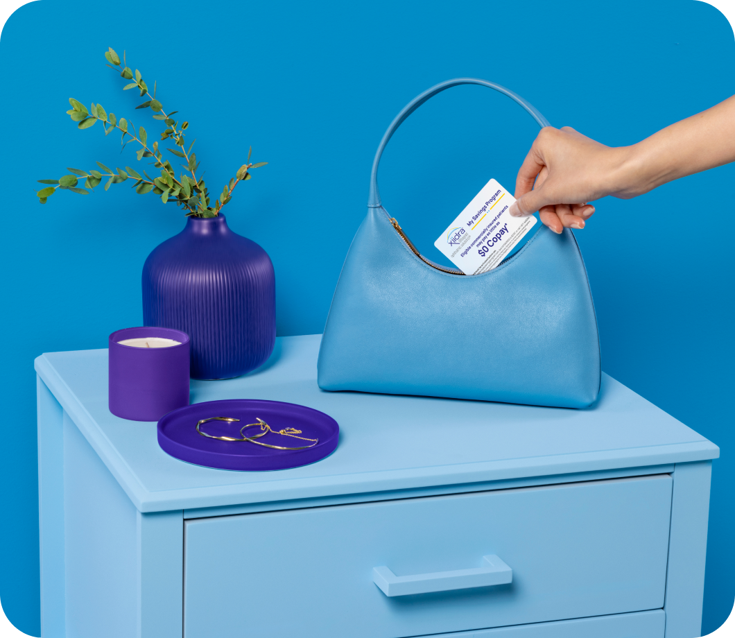 Hand holding a Xiidra Savings Program card above a blue purse on a blue side table