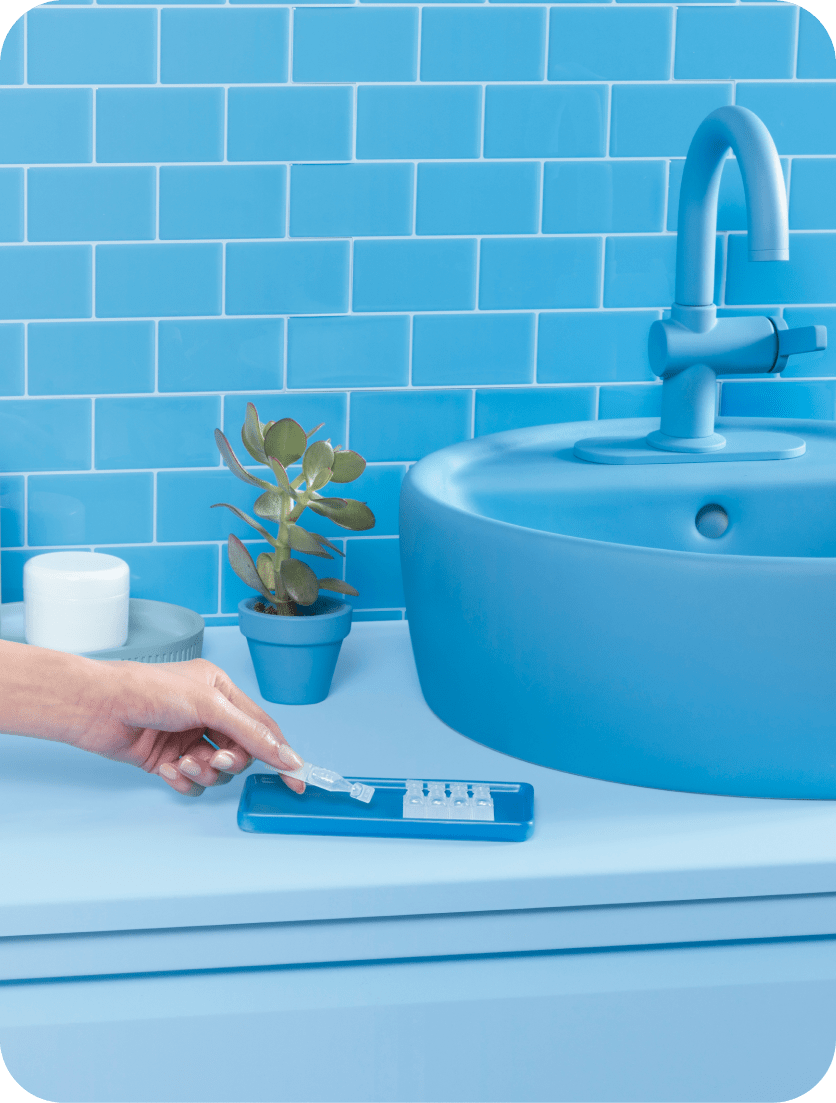 A hand placing a Xiidra eye drop vial in a tray next to the sink